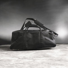 Black duffel bag on a textured surface with a dark background